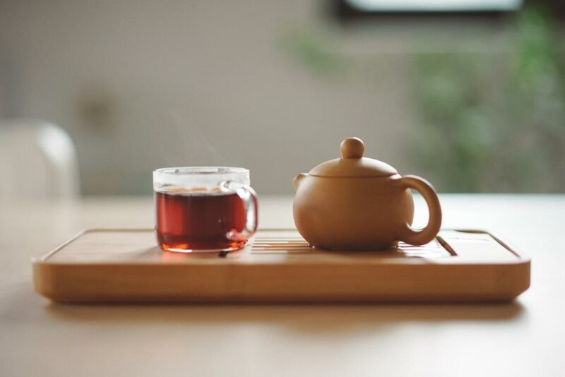xícara com chá de sene em uma bandeja de madeira com um bule